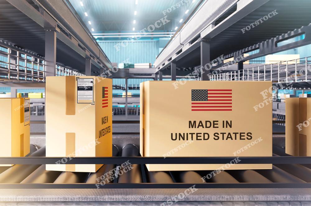На изображении коробки с маркировкой «Made in United States» движутся по автоматизированному конвейеру в просторном складском помещении. Конвейерная система демонстрирует технологические решения для оптимизации производства и логистики. Снимок иллюстрирует высокоэффективные процессы упаковки и доставки.